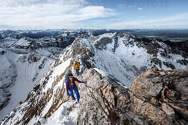 Two mountaineers on a rocky snow-covered ridge, the path is secured by a wire rope
