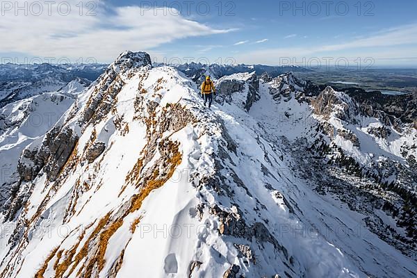 Climbers on a narrow rocky snowy ridge, behind peak crow