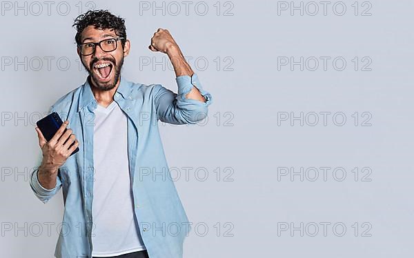 Excited man winning a prize from his cellphone. Excited handsome man looking at smartphone celebrating something. Happy person holding a smartphone and celebrating,