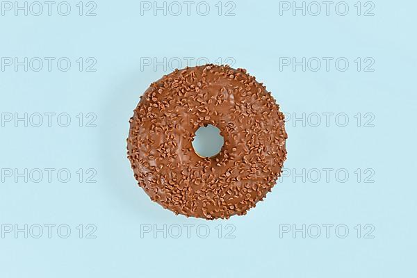 Donut glazed with chocolate with brown sprinkles on light blue background,