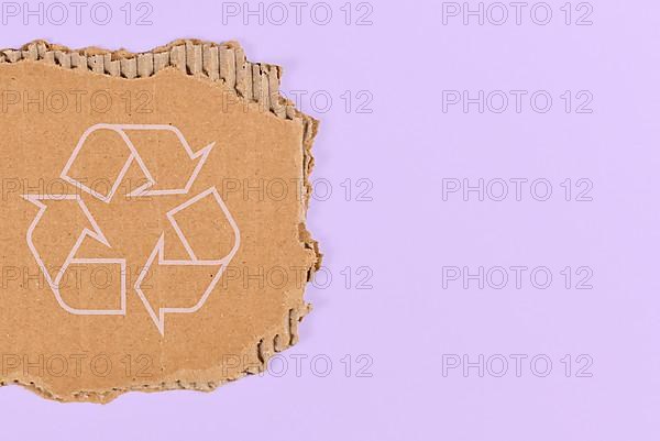 Piece of cardboard with recycling arrow sign on violet blue background with copy space,