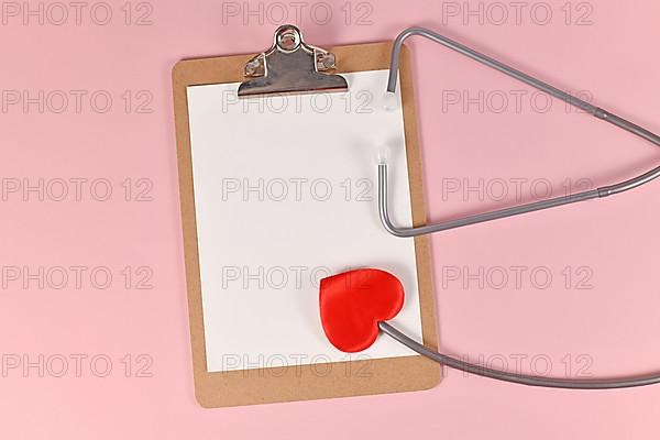 Heart shaped stethoscope with empty clipboard on pink background,