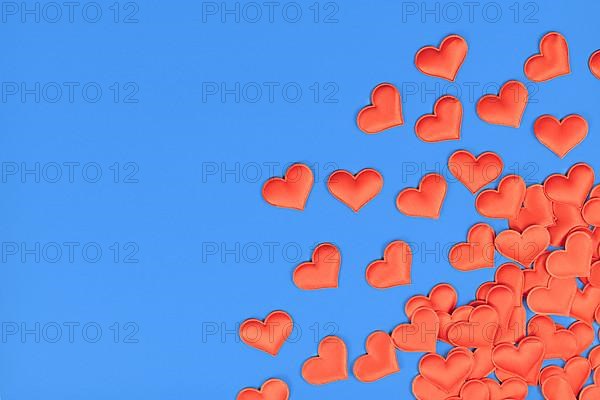 Red heart shaped confetti in corner of blue background with empty copy space,
