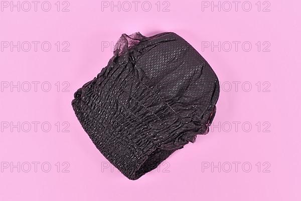 Black folded diaper for adult women on pink background,