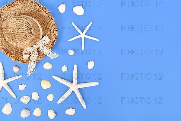 White starfish, seashells and summer straw hat on side of blue background with copy space