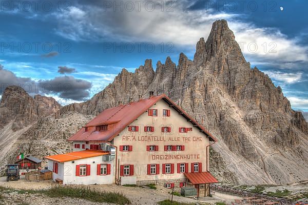 Mountain hut Dreizinnenhuette with rock massif Paternkofel in the evening, moon behind