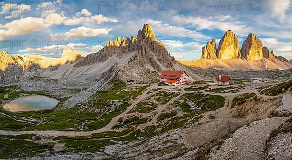 View of mountain hut Dreizinnenhuette and chapel with mountain lake rock massif Paternkofel and mountains three peaks in the sunset, panorama