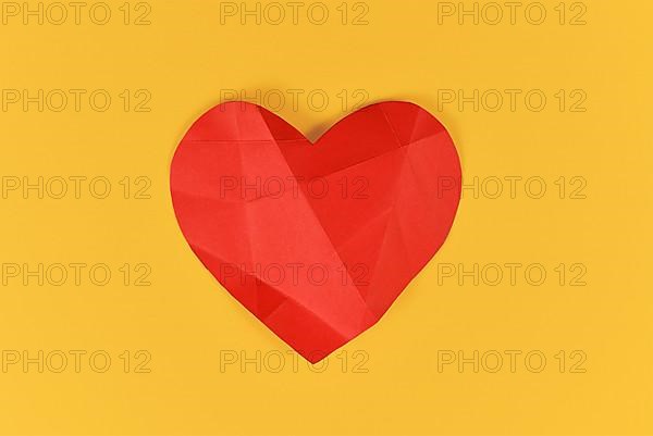 Red paper heart with folding lines on yellow background. Concept for broken or sick heart,