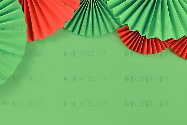 Red and Green paper craft rosettes in traditional Christmas colors at top of green background with empty copy space,