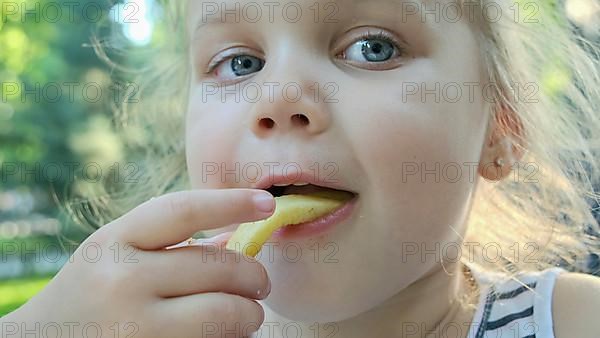 Little girl eat french fries. Close-up of blonde girl takes potato chips with her hands and tries them sitting in street cafe on the park. Odessa, Ukraine