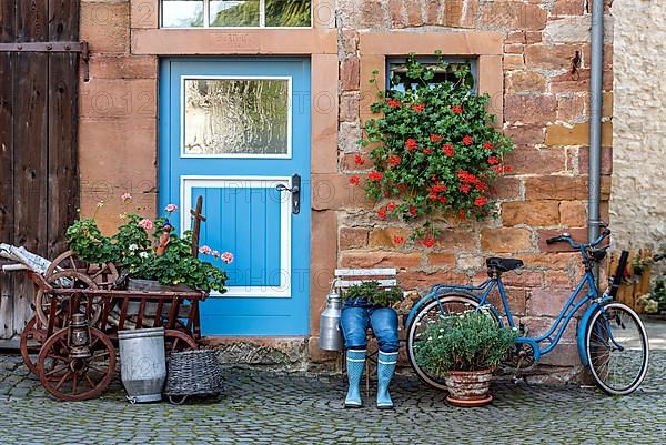 Curious decoration on a front door, blue jeans trousers in rubber boots with flower pot