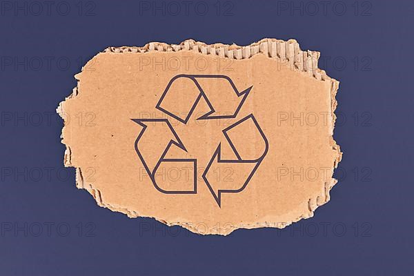 Piece of cardboard with recycling arrow sign on dark blue background,