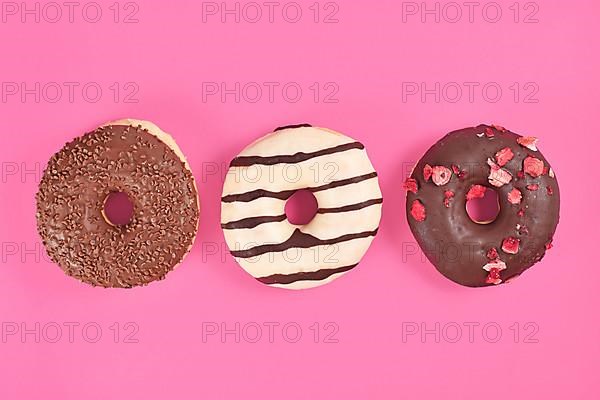 Donuts with chocolate glazing and sprinkles in a row on pink background,