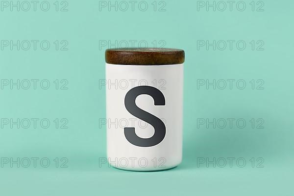 White salt shaker with wooden lid and letter S on green background,