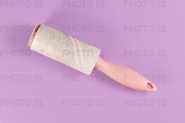 Used fluff roller for cleaning clothes on violet background,
