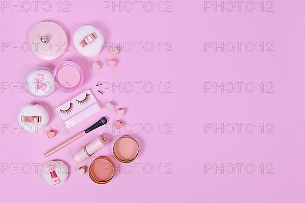 Pink makeup beauty products like brushes, powder or lipstick on side of pastel pink background with empty copy space