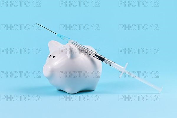 Corona virus vaccine expenses or cash infusion concept with white piggy bank and syringe on blue background,