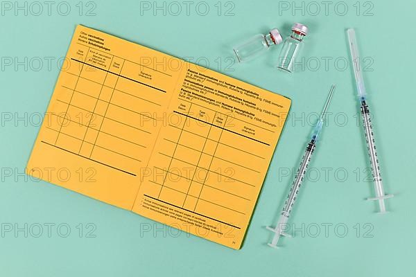 Concept for vaccination with syringes, vials and empty yellow international certificate of vaccination with German and English text on green background