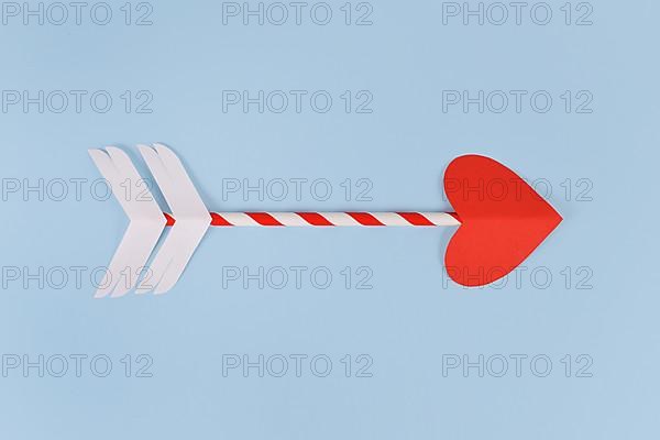 Simple paper cupid love arrow with heart shaped tip on blue background,
