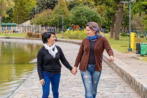 Lesbian couple in a park holding hands walking looking at each other,