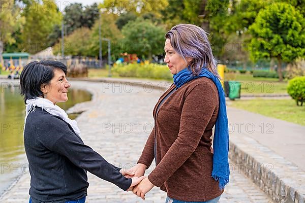 Lesbian couple in a park holding hands looking at each other,