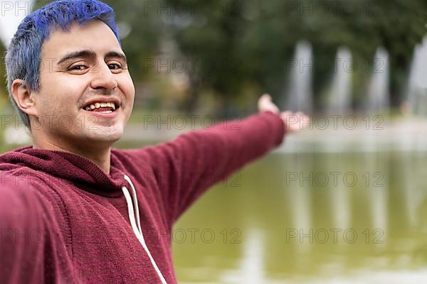 Active young Caucasian latin gay man taking selfie showing around at a lake. Outdoor adventure concept,