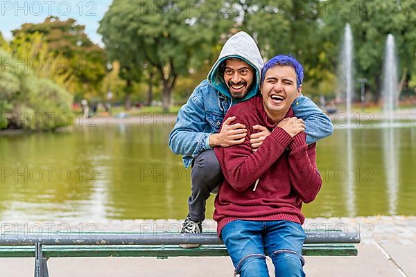 Gay Latino male couple sitting on a bench in a park laughing,