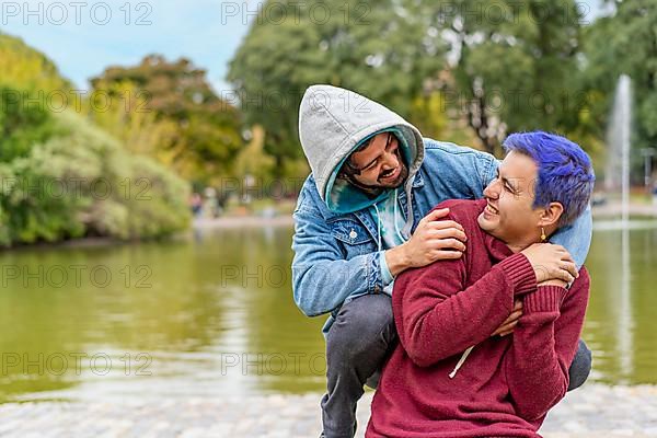 Gay Latino male couple sitting on a bench in a park, looking at each other smiling