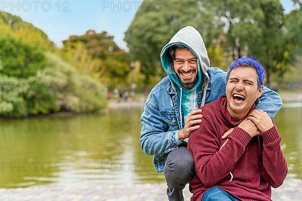 Gay Latino male couple sitting on a bench in a park laughing,