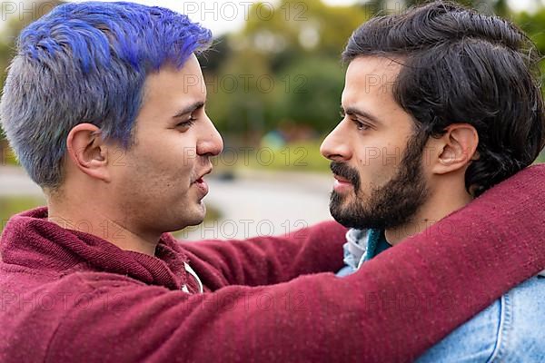 Latin gay couple hugging in a park looking at each other about to kiss,