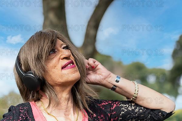 Trans woman listening to music outdoors with headphones. Expression of happiness, winning attitude. Copy space