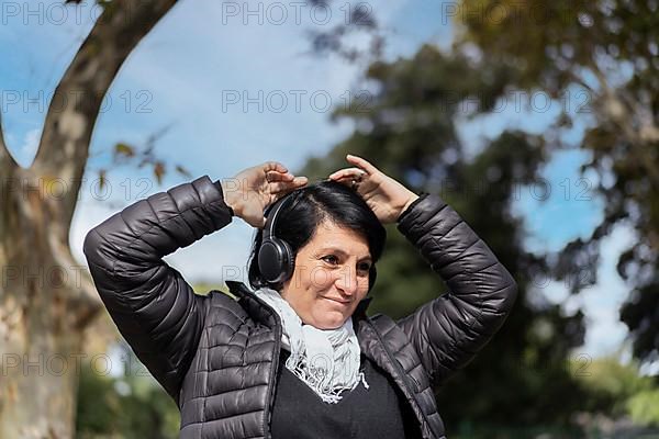 Latin woman listening to music outdoors with headphones. Expression of happiness, winning attitude. Copy space