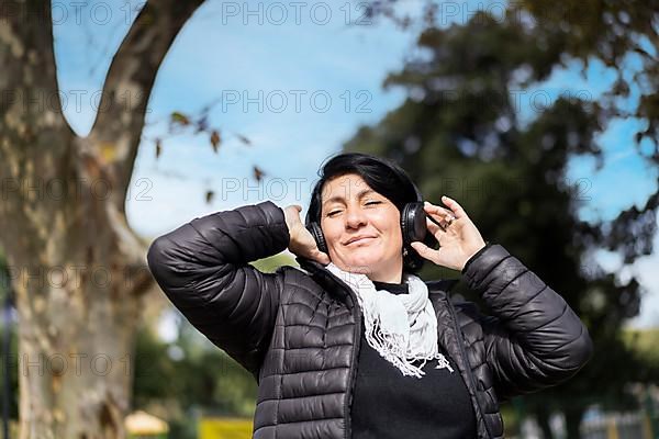 Latin woman listening to music outdoors with headphones. Expression of happiness, winning attitude. Copy space