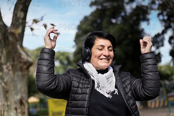 Latin woman listening to music outdoors with headphones. Expression of happiness, winning attitude. Copy space