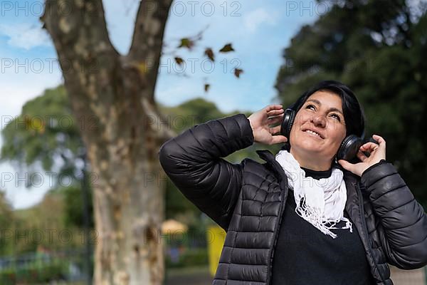 Latin woman listening to music outdoors with headphones. Expression of happiness, winning attitude. Copy space