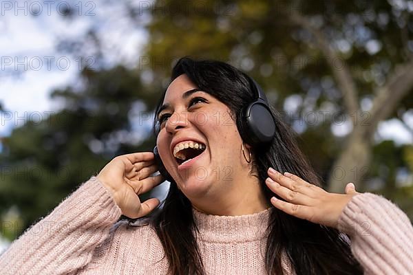 Young latin woman listening to music outdoors with headphones. Expression of happiness, winning attitude. Copy space
