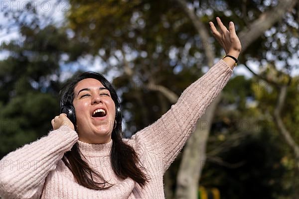 Young latin woman listening to music outdoors with headphones. Expression of happiness, winning attitude. Copy space