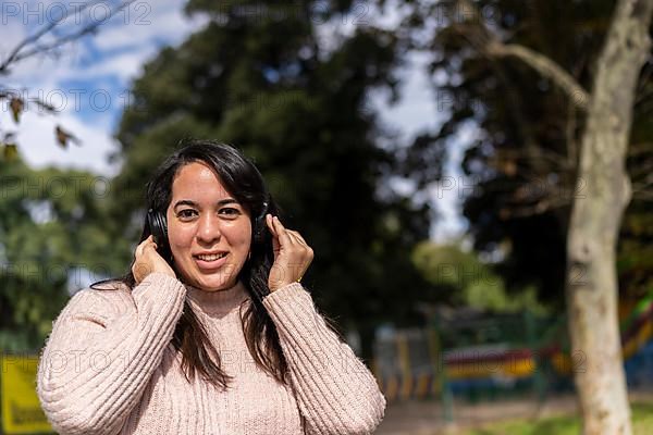 Young latin woman listening to music outdoors with headphones. Expression of happiness, winning attitude. Copy space