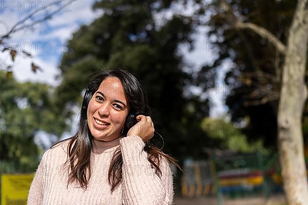 Young latin woman listening to music outdoors with headphones. Expression of happiness, winning attitude. Copy space