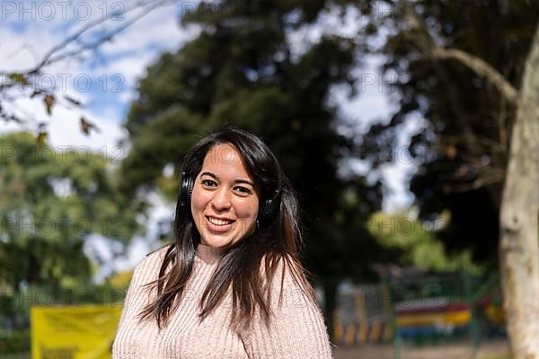 Young latin woman listening to music outdoors with headphones. Expression of happiness, winning attitude. Copy space