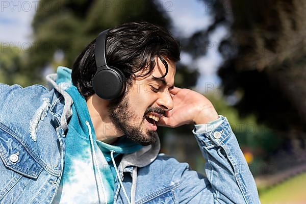 Young latin man listening to music outdoors with headphones. Expression of happiness, winning attitude