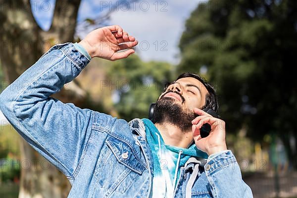 Young latin man listening to music outdoors with headphones. Expression of happiness, winning attitude