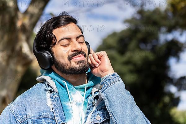 Young latin man listening to music outdoors with headphones. Expression of happiness, winning attitude