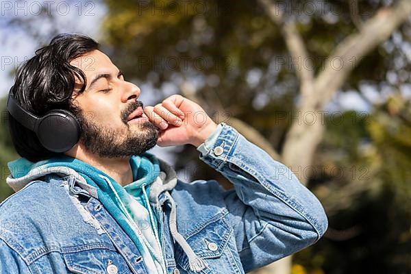 Young latin man listening to music outdoors with headphones. Expression of happiness, winning attitude