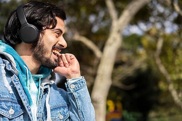 Young latin man listening to music outdoors with headphones. Expression of happiness, winning attitude