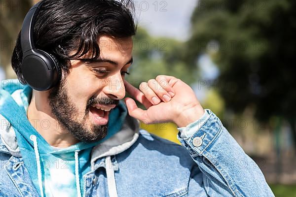 Young latin man listening to music outdoors with headphones. Expression of happiness, winning attitude