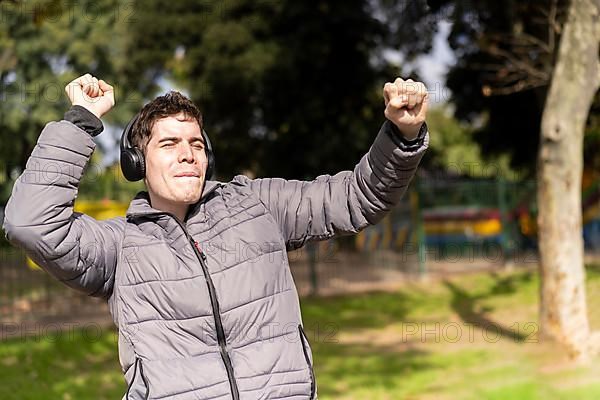 Young latin man listening to music outdoors with headphones. Expression of happiness, winning attitude