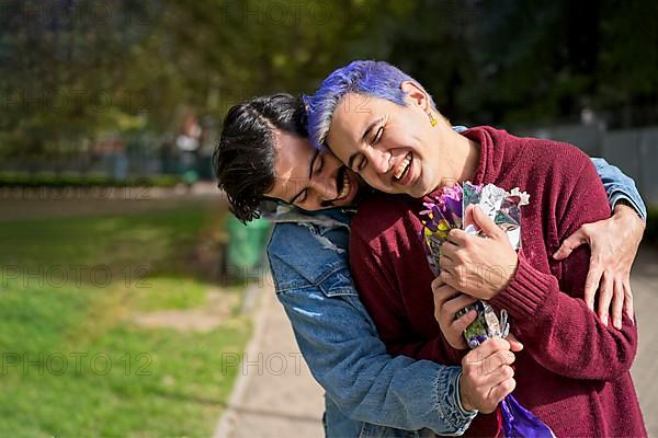 Couple of Latino gay men in a park embracing each other. One surprising the other with a bouquet of flowers as a gift,