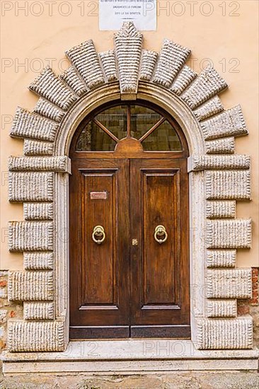 Round arched house entrance door framed with cream-coloured stones, Montefollonico