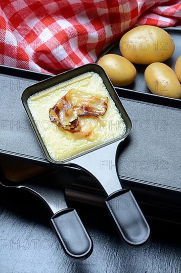 Raclette, melted raclette cheese with bacon in pans and ingredients